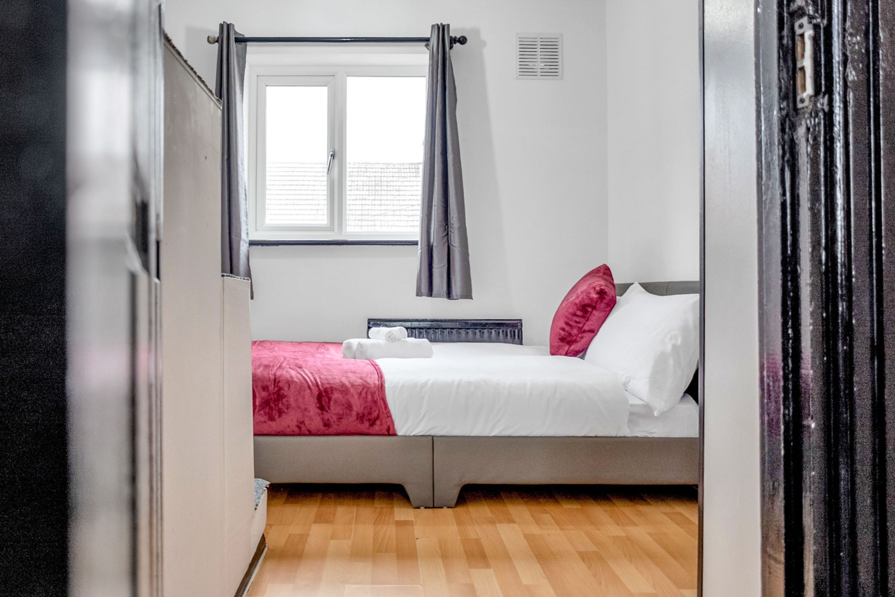 Un llit individual amb una edredó blanca i rosa, una finestra amb cortines i un radiador.