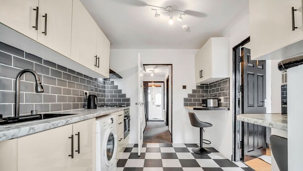 A modern kitchen with a checkered floor, white cabinetry, and a built-in washing machine. - Spacious 4-bedroom Haven in Orpington Retreat (Orpington)