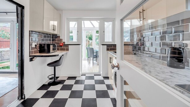 Una cucina moderna con pavimento a scacchi, mobili bianchi e un piano di lavoro nero.