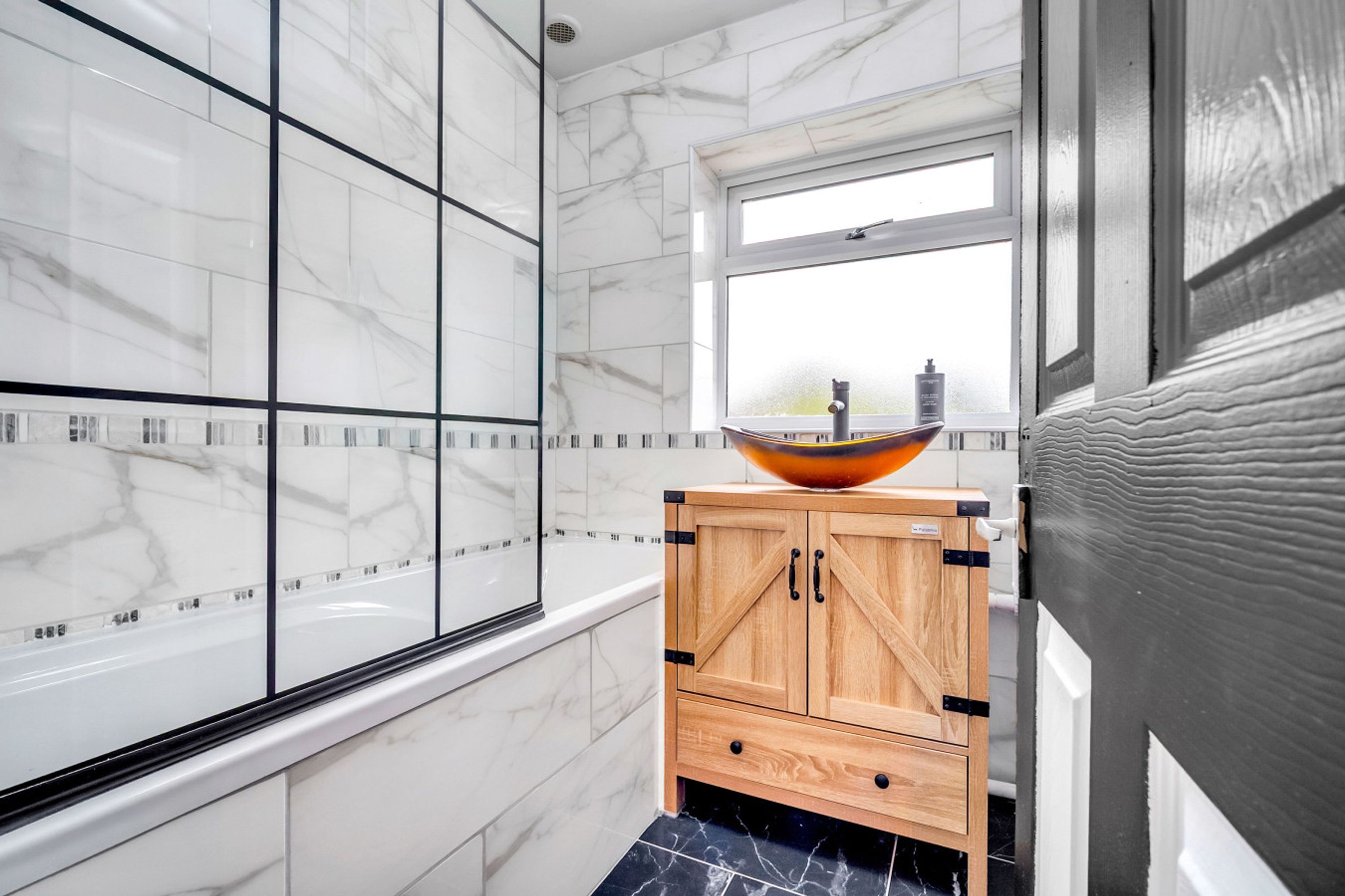 Une salle de bain avec un mur en marbre, un meuble en bois et une fenêtre.