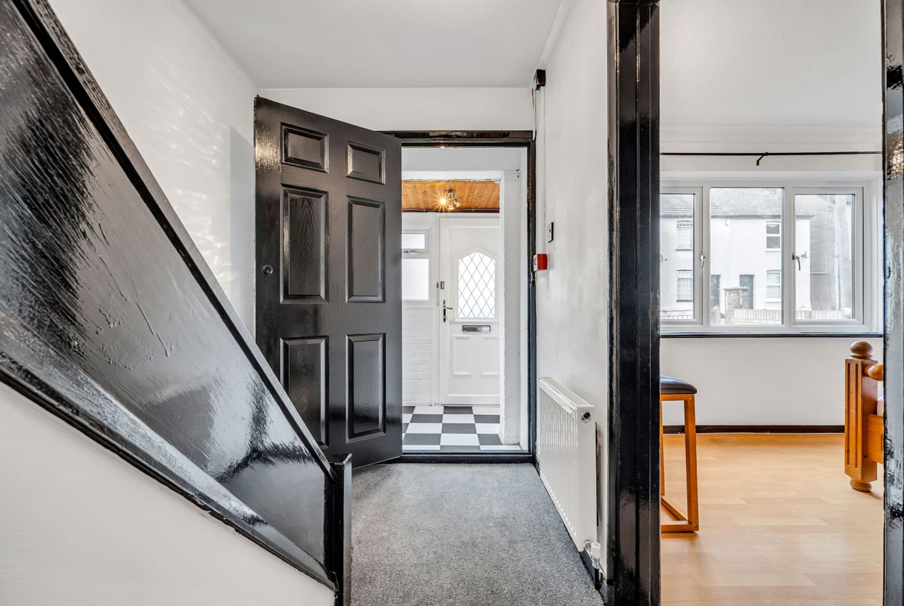 A hallway with a black door, a checkered floor, and a window with a view of buildings.