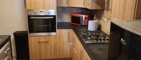 Une cuisine compacte dotée de meubles en bois, d’une cuisinière à gaz, d’un four à micro-ondes, d’un four traditionnel et d’un lave-linge.