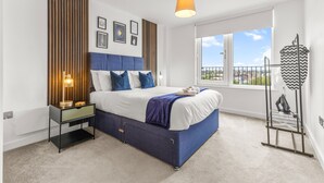 Ein modernes Schlafzimmer mit Bett, Nachttisch, Lampe und Blick auf die Stadt durch das Fenster.