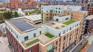 Ein modernes Gebäude mit Dachgarten und Solaranlage, umgeben von weiteren Hochhäusern.