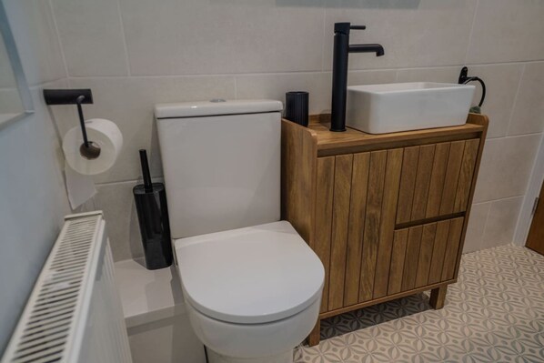 A modern bathroom with a toilet, a wooden cabinet, a sink, and a radiator. - Modern 3BR Flat in Central Plymouth Free Parking Sleeps 6 (Plymouth)