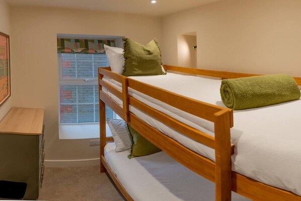 A bunk bed with a green towel, a wooden desk, a window with a view, and a framed picture on the wall. - Modern 3BR Flat in Central Plymouth Free Parking Sleeps 6 (Plymouth)