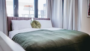 A hotel room with a bed, curtains, a window, and a view of buildings outside. - Elizabeth Line Retreat Modern 2BR Flat in Hayes (Hayes)