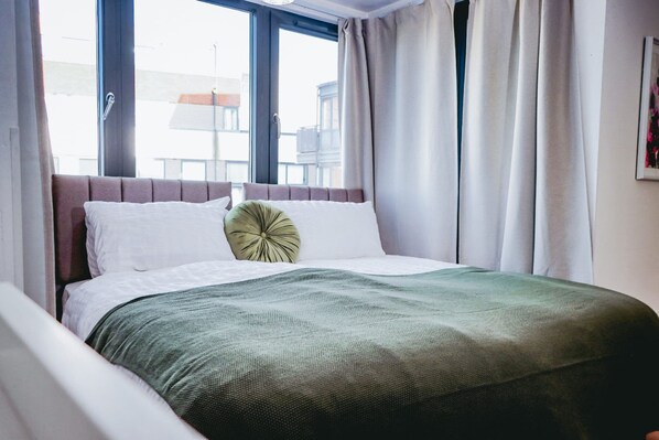 A hotel room with a bed, curtains, a window, and a view of buildings outside. - Elizabeth Line Retreat Modern 2BR Flat in Hayes (Hayes)