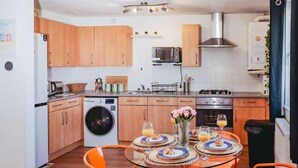 A compact kitchen with wooden cabinets, a washing machine, a microwave, and a gas stove. - Elizabeth Line Retreat Modern 2BR Flat in Hayes (Hayes)
