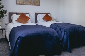 Two single beds with headboards, white bedding, and dark blue bedspreads. - Elizabeth Line Retreat Modern 2BR Flat in Hayes (Hayes)