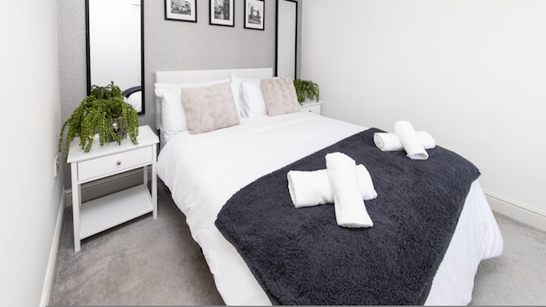 A bedroom with a bed, a nightstand, a mirror, and framed pictures on the wall. - 3BR Thames Retreat Heathrow 10min Train 5min (Egham)