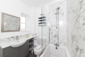 Une salle de bain moderne avec un lavabo blanc, une douche en verre et des murs à motifs de marbre.