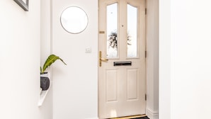 A white door with a brass handle, a round mirror, and a potted plant on a shelf. - 3BR Thames Retreat Heathrow 10min Train 5min (Egham)