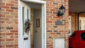 A brick building with a white door, a red car parked outside, and a black lantern on the wall. - 3BR Thames Retreat Heathrow 10min Train 5min (Egham)