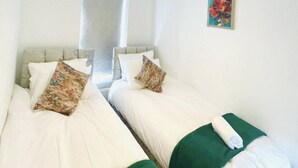 Een hotelkamer met twee bedden, elk voorzien van witte lakens en groene sierkussens.