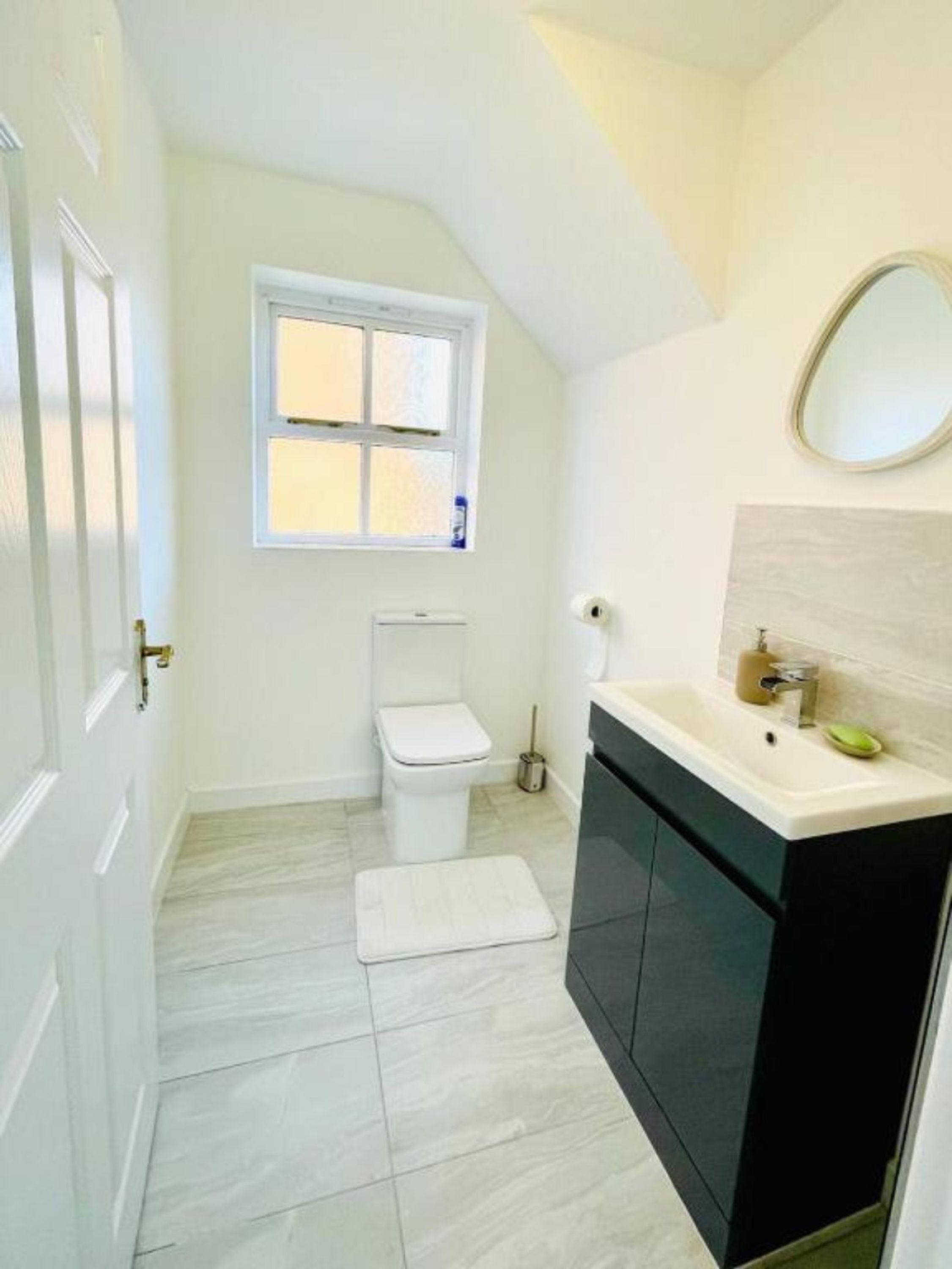 A bathroom with a toilet, a window, a sink, and a mirror.