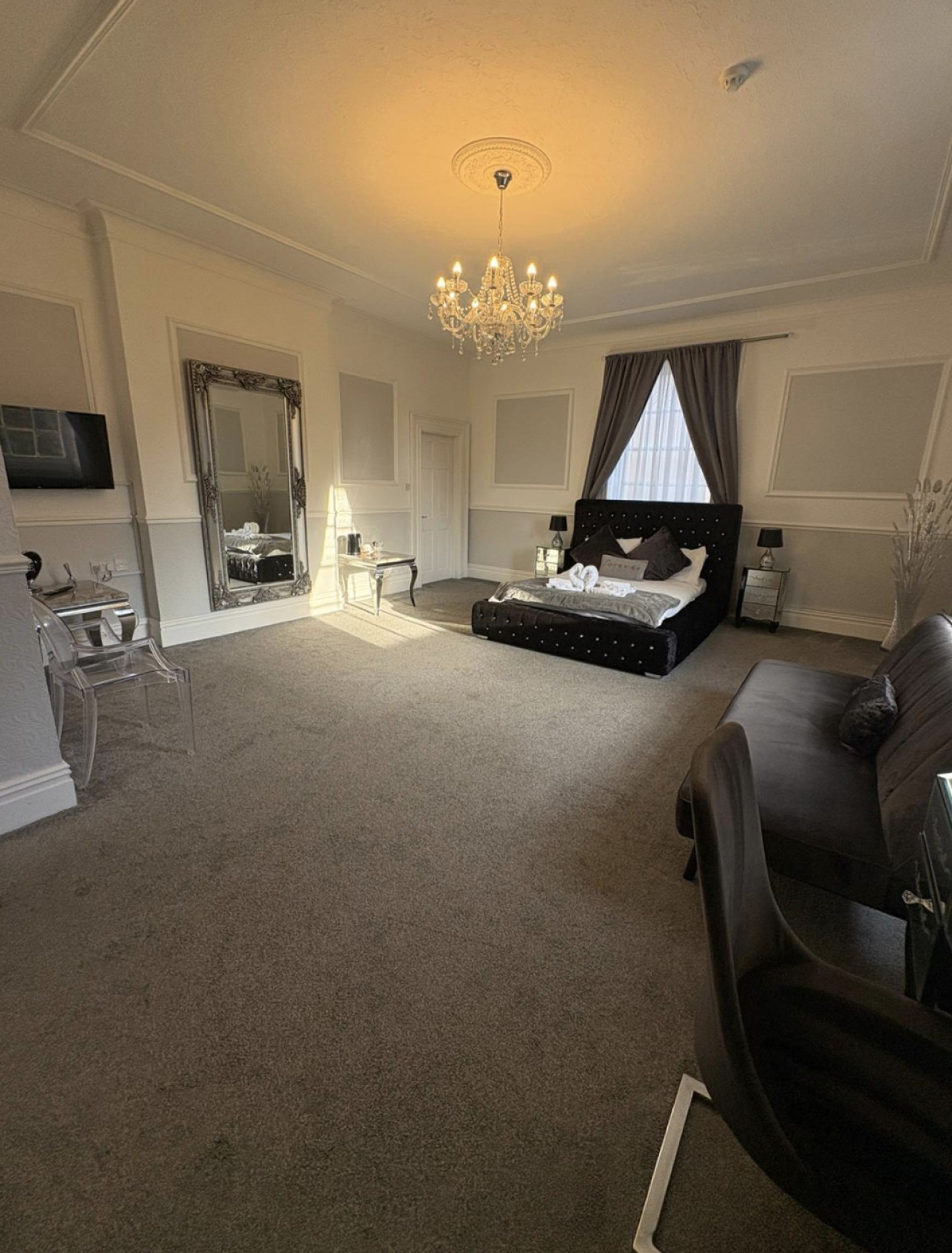 A spacious bedroom with a large bed, a chandelier, a mirror, and a television.
