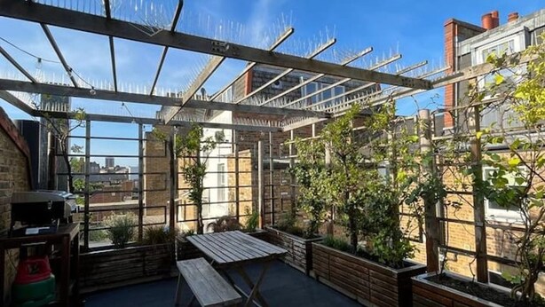 A rooftop terrace with a wooden table and chairs, a pergola structure, and potted plants. - Stylish East London Retreat With Private Terrace Fast Wifi (London)