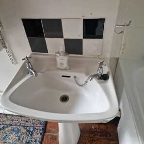 Ein weißes Waschbecken mit zwei Wasserhähnen, einer Seifenspender und einem Abfluss.