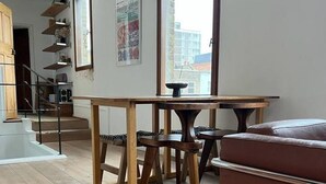 A modern living room with a wooden dining table, a sofa, and a staircase leading to an upper floor. - Stylish East London Retreat With Private Terrace Fast Wifi (London)