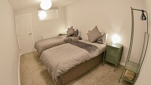 Un dormitorio con dos camas, un radiador, una mesita de noche verde y un perchero.