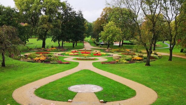 Un jardín formal con un sendero central, parterres simétricos y un césped circular.