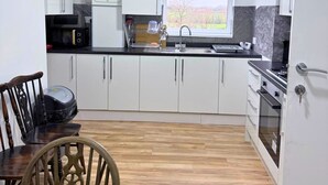 Una cocina moderna con armarios blancos, encimera negra, ventana con vistas y zona de comedor con mesa y sillas de madera.
