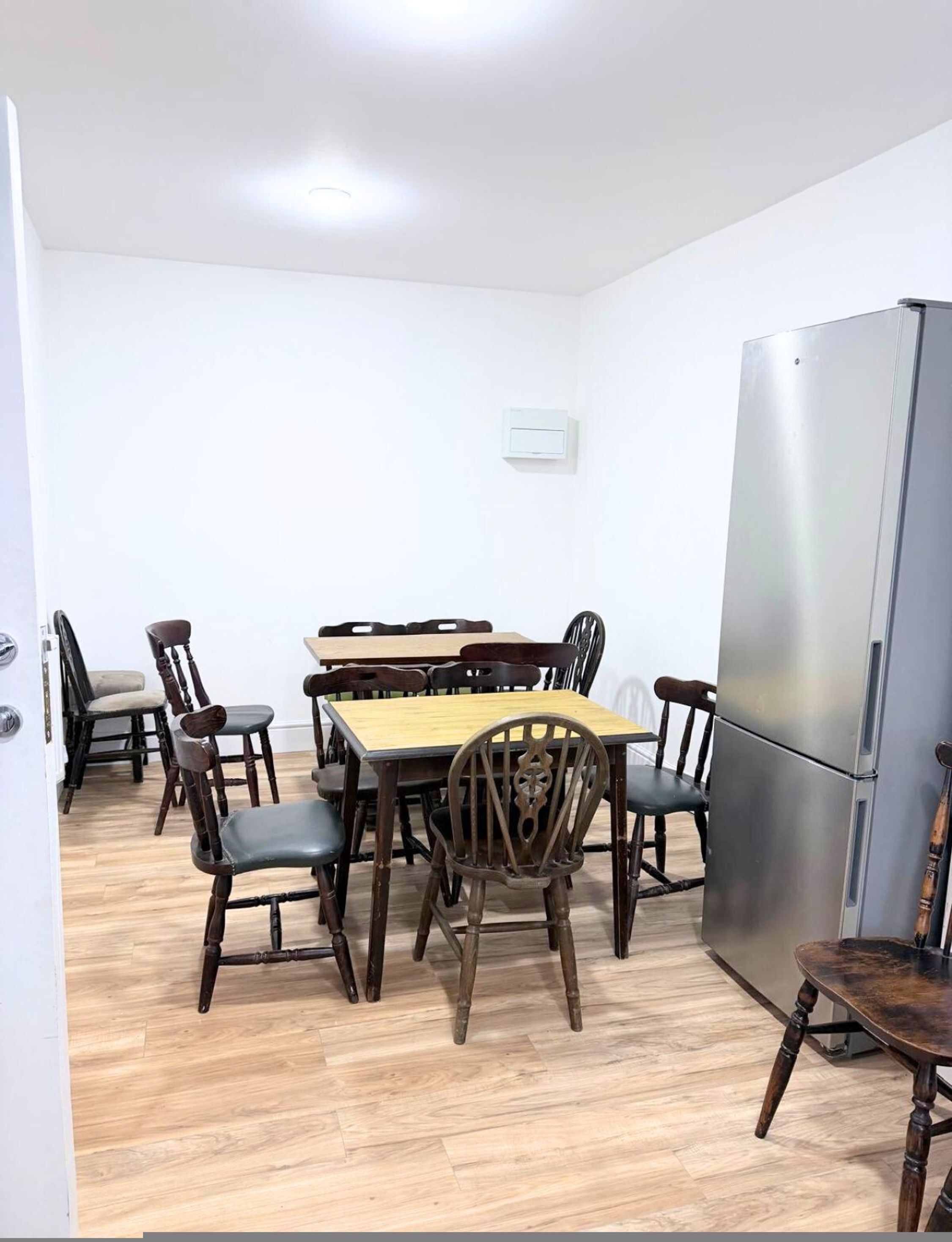 A compact dining area with a wooden table and chairs, a stainless steel refrigerator, and a light switch on the wall.