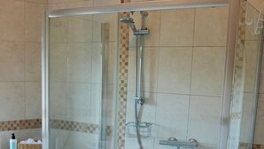Une cabine de douche fermée par des parois en verre, équipée d’un pommeau de douche fixe, d’un pommeau de douche amovible et d’un robinet amovible.