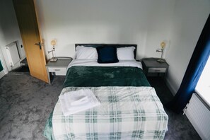Ein Schlafzimmer mit einem Bett, zwei Nachttischen, einer Heizung, einer Tür und einem Fenster mit Vorhängen.