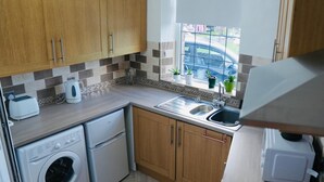 Une cuisine compacte avec des meubles en bois, un lave-linge encastré, un évier et une fenêtre donnant sur la rue.