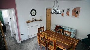 Un coin repas avec une table et des chaises en bois, une horloge au mur et une porte donnant sur une autre pièce.