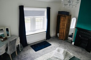 Ein Schlafzimmer mit Fenster, Heizkörper, Holzschrank, Spiegel, Schminktisch und Teppich.