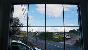 Une route de campagne avec une voiture blanche garée sur le bord, un rond-point en contrebas et un mur de pierres sur la gauche.