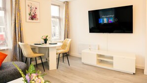 Uma sala de estar moderna com uma televisão de tela plana, uma mesa de jantar, cadeiras e um móvel de entretenimento branco.
