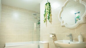 Casa de banho com banheira, sanita, lavatório e espelho com moldura decorativa.