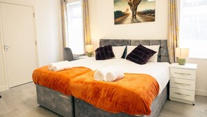 Quarto de hotel com uma cama grande, duas mesas de cabeceira, cabeceira, um quadro na parede e uma porta.