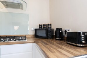 Een keuken met een gasfornuis, een magnetron, een koffiezetapparaat en een broodrooster.