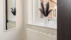 Una ventana con un radiador blanco debajo y un florero negro con plumas en el alféizar.