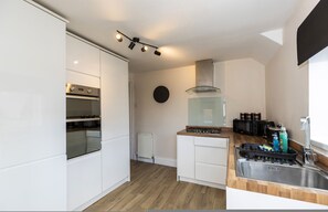 Een moderne keuken met witte kastjes, een ingebouwde oven, een gasfornuis en een roestvrijstalen spoelbak.