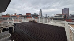 Terraza en la azotea con vistas a un paisaje urbano, que incluye varios edificios y un cielo nublado.