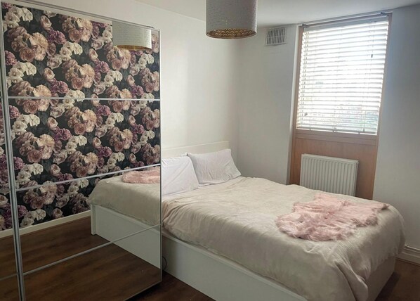 Ein Schlafzimmer mit Bett, Spiegel, Fenster mit Jalousien und Heizkörper.