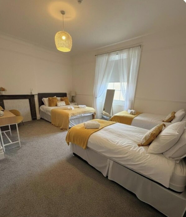 A hotel room with two beds, a desk, a chair, a hanging light fixture, and a window with curtains. - Room 10 - Manor Park Country House Wales (Swansea)