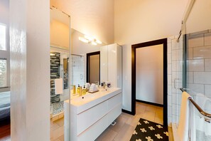 Un baño moderno con un tocador blanco, un espejo grande y una cabina de ducha de vidrio.