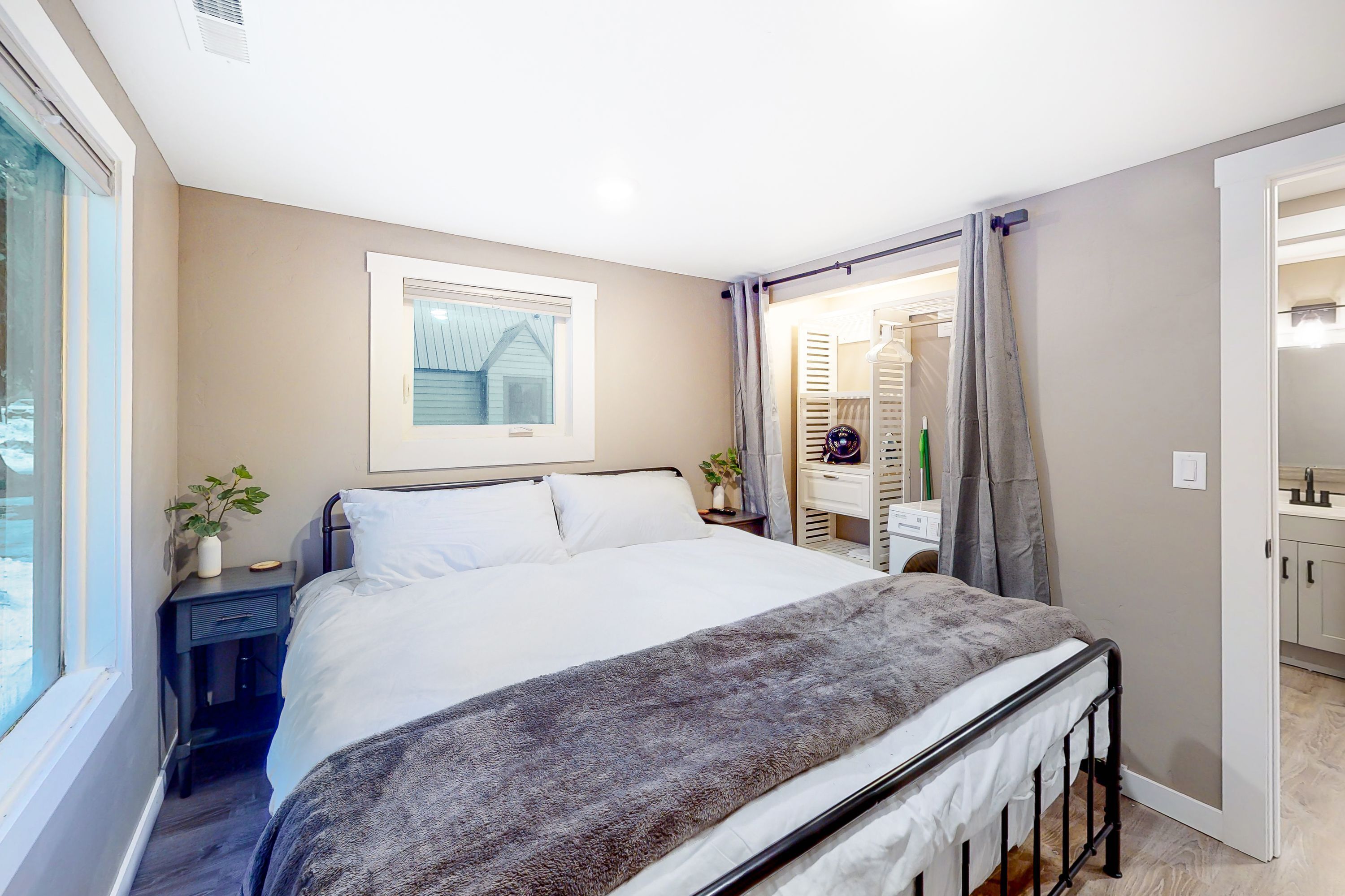 A bedroom with a bed, bedside tables, a window, and a view of a bathroom.