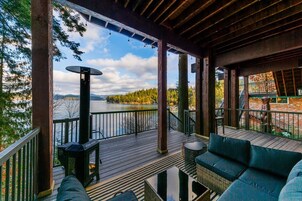 Una terraza techada con vistas a un lago, mobiliario exterior y una fogata.