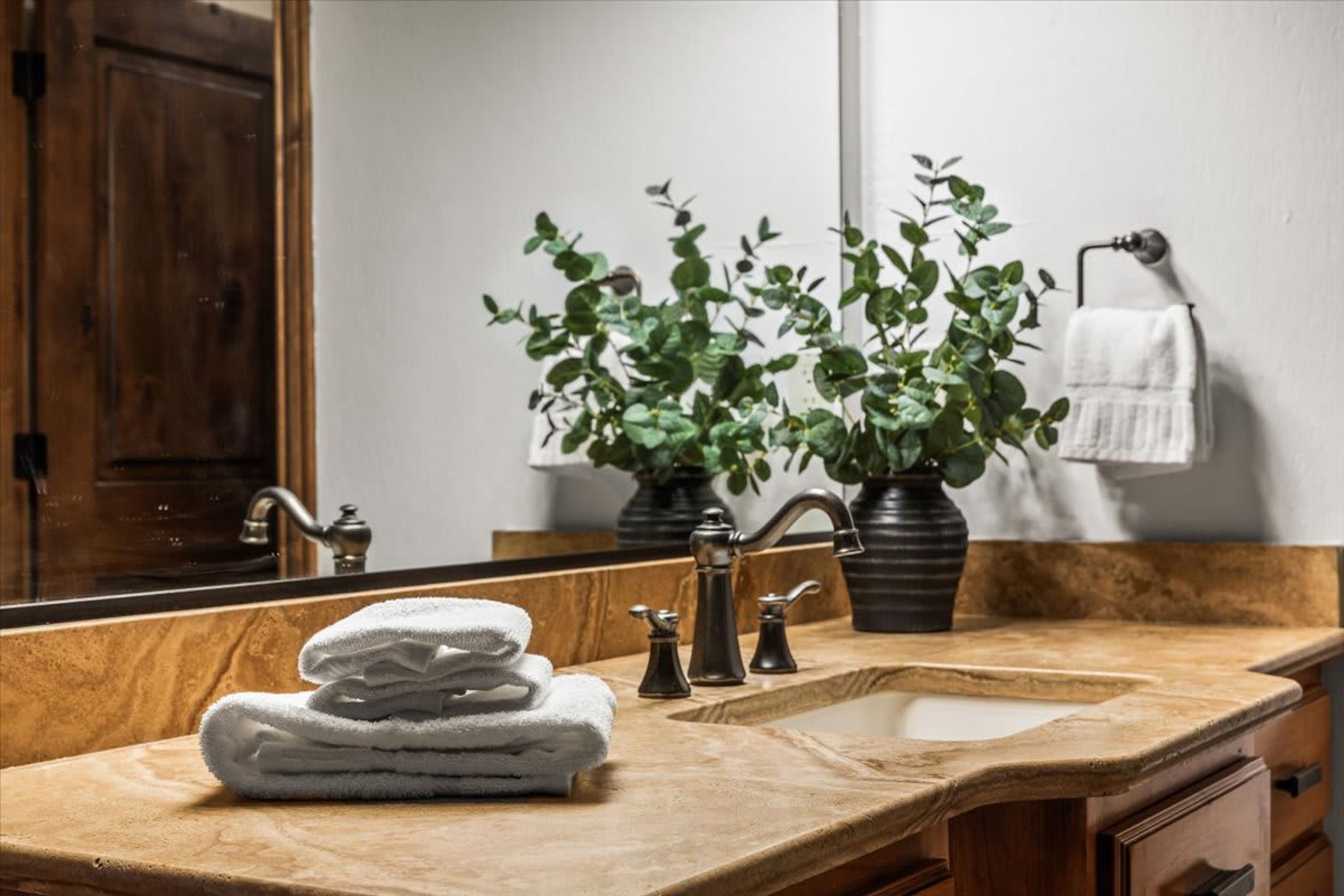 Un baño con tocador de madera, lavamanos, espejo, una pila de toallas y una planta en maceta.