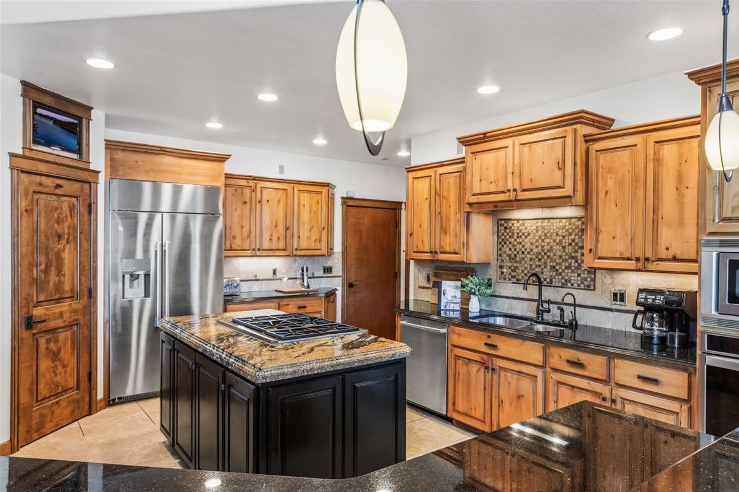 A modern kitchen with wooden cabinets, stainless steel appliances, granite countertops, and pendant lighting.