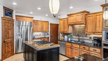 A modern kitchen with wooden cabinets, stainless steel appliances, granite countertops, and pendant lighting.