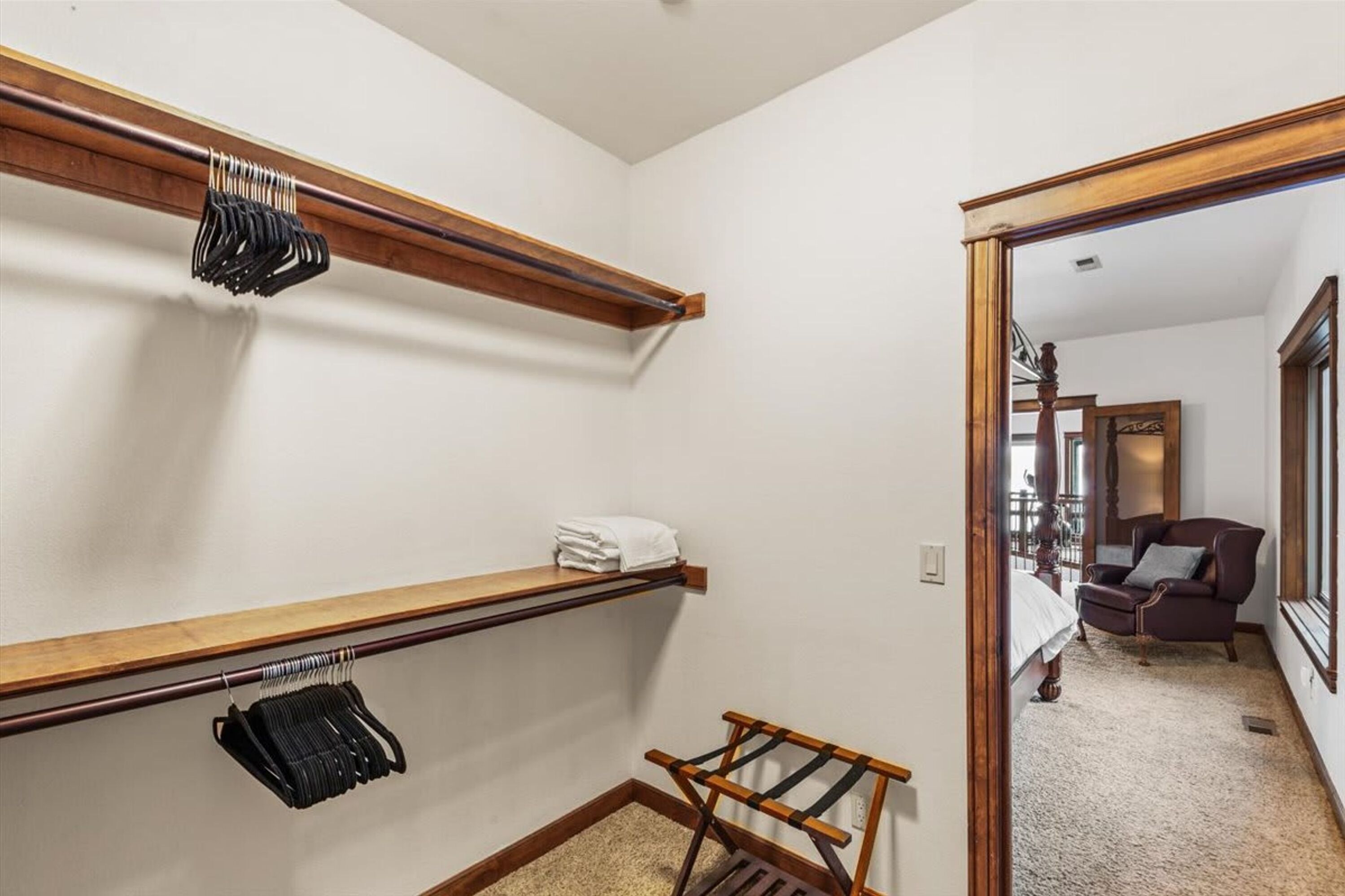 A walk-in closet with wooden shelves, a hanging rack, and a small rack with folded towels.